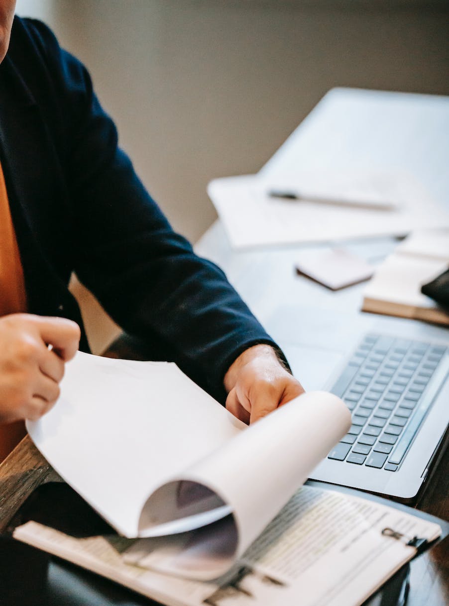 a person looking through papers in front of an open laptop