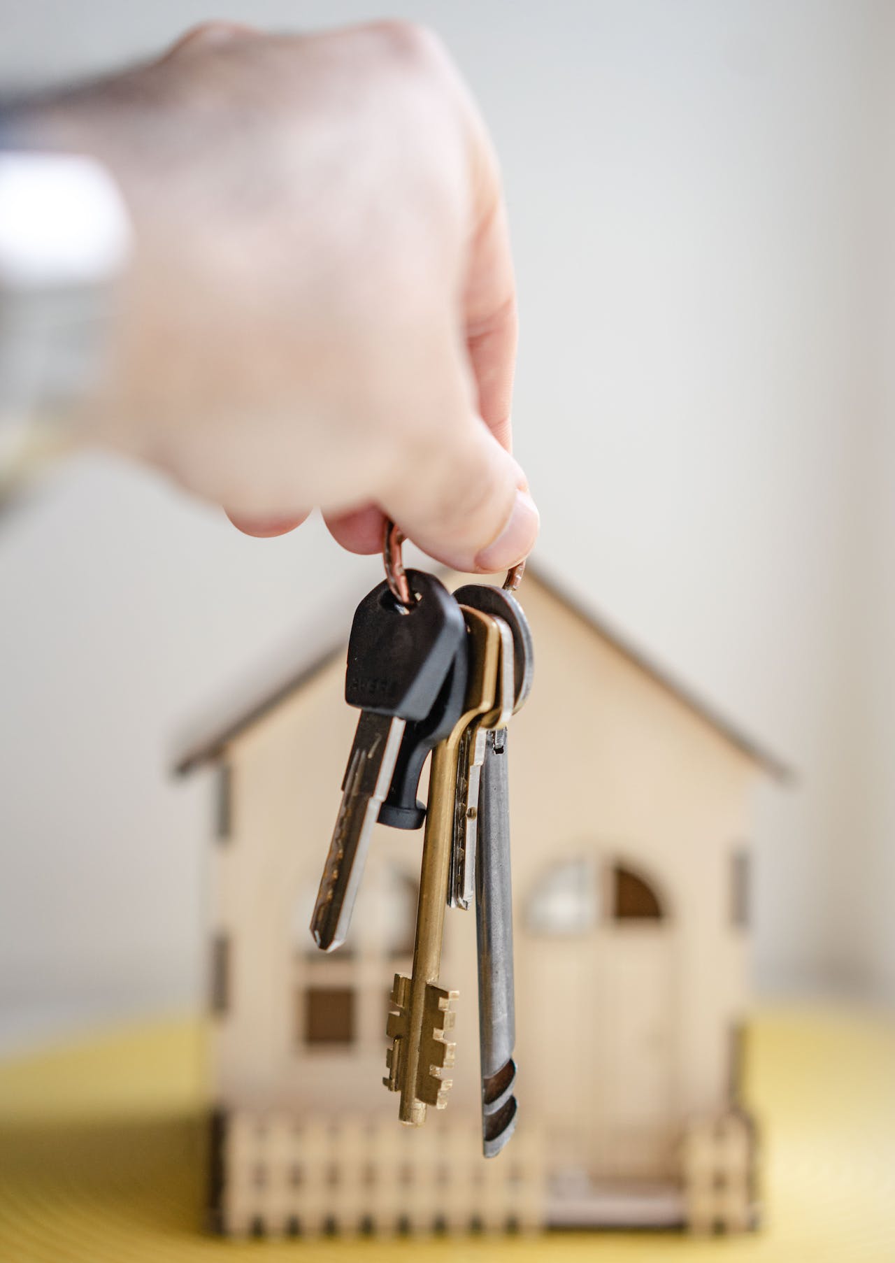 a person holding keys with a wooden model of a house in the background