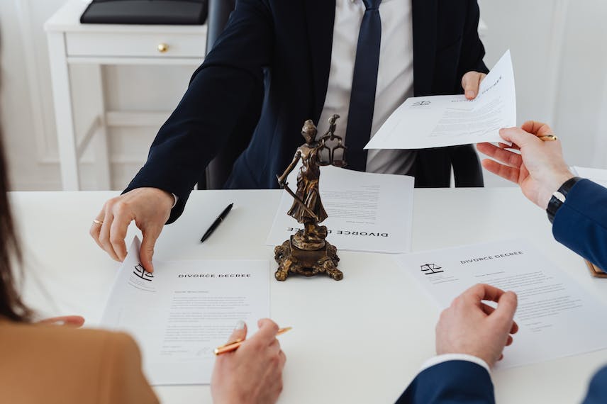 a man in a suit sitting at his desk and handing papers to someone sitting across from him